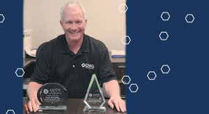 Smiling man with two awards on desk.
